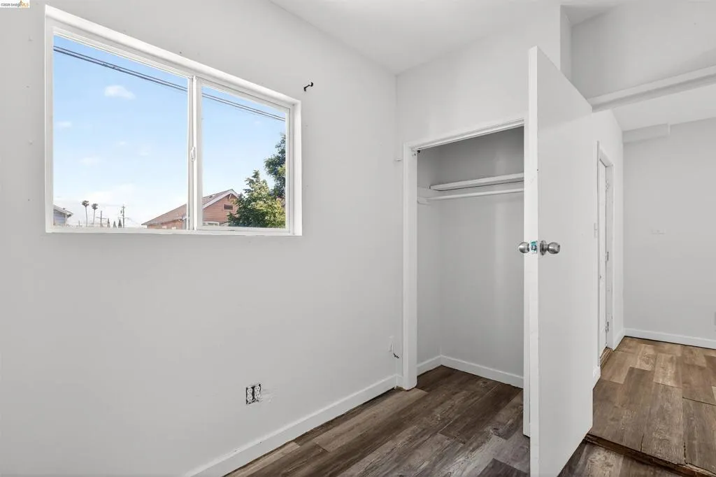 Room featuring a large window, wood-finish flooring, white walls, and a closet with a hanging rod