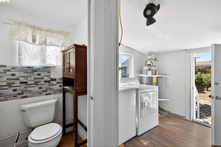 Laundry area with washer and dryer, water heater, wood-finish flooring, and exterior access