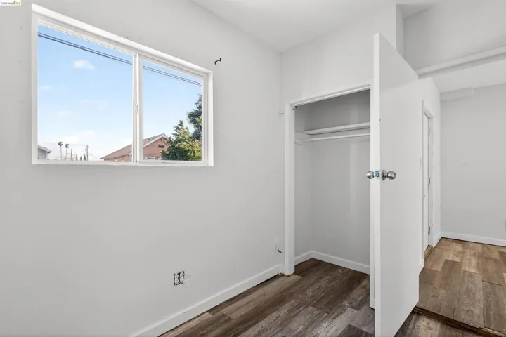 Room featuring a large window, wood-finish flooring, white walls, and a closet with a hanging rod