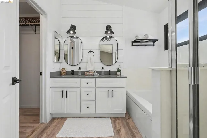 Bathroom with double vanity, light wood-style floors, a bath, and a spacious closet
