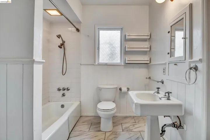 Full bath with washtub / shower combination, wainscoting, and light marble finish flooring