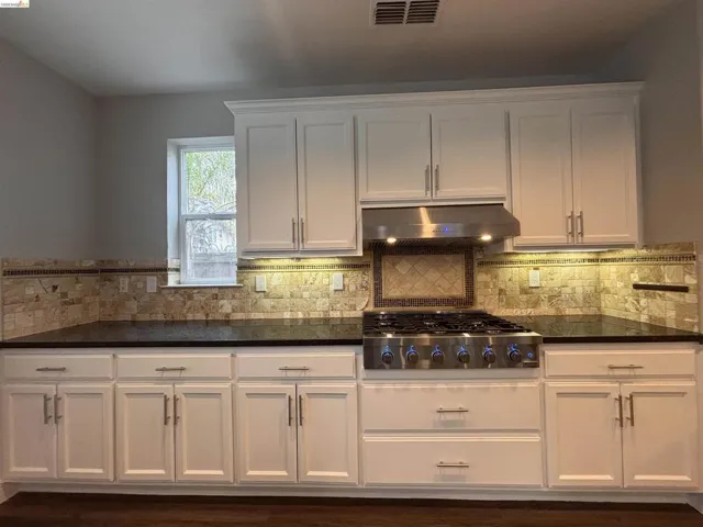 Kitchen featuring white cabinets, stainless steel gas cooktop, and dark stone countertops