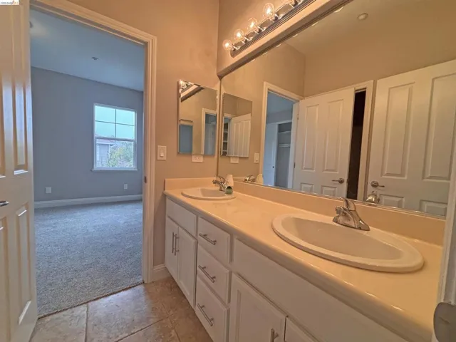 Bathroom featuring light colored carpet, double vanity, and light tile patterned floors