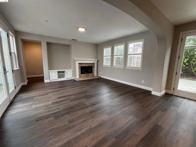 Unfurnished living room featuring dark wood-type flooring, a fireplace with raised hearth, and arched walkways