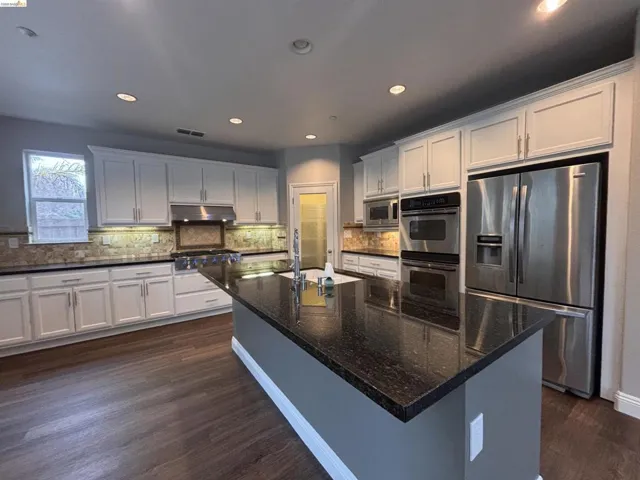 Kitchen featuring stainless steel appliances, dark wood-type flooring, white cabinetry, dark stone counters, and recessed lighting