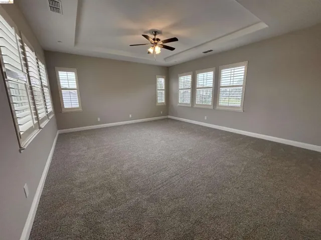 Spare room featuring a raised ceiling, dark carpet, and ceiling fan