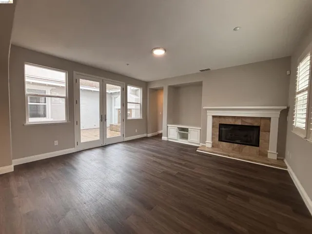 Unfurnished living room with french doors, dark wood-style flooring, and a tile fireplace