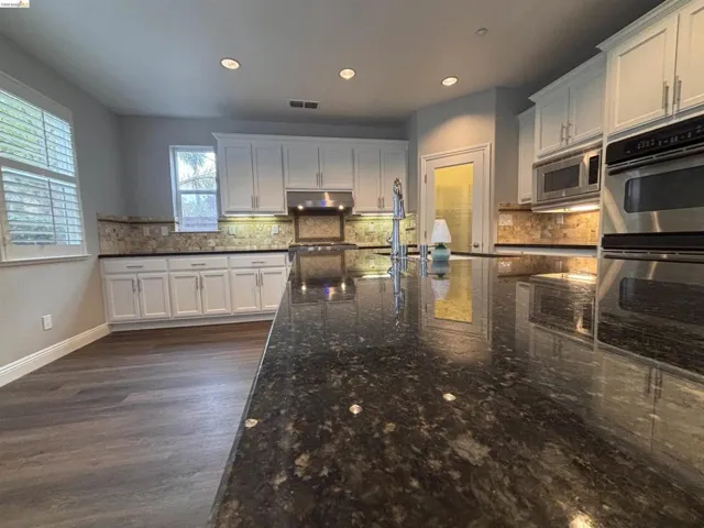 Kitchen with white cabinets, stainless steel appliances, tasteful backsplash, recessed lighting, and dark stone counters