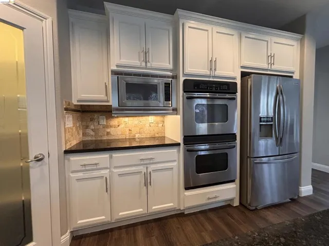 Kitchen featuring white cabinetry, stainless steel appliances, dark wood-type flooring, backsplash, and dark stone counters