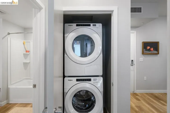 Laundry room with stacked washer and clothes dryer and light wood-style flooring