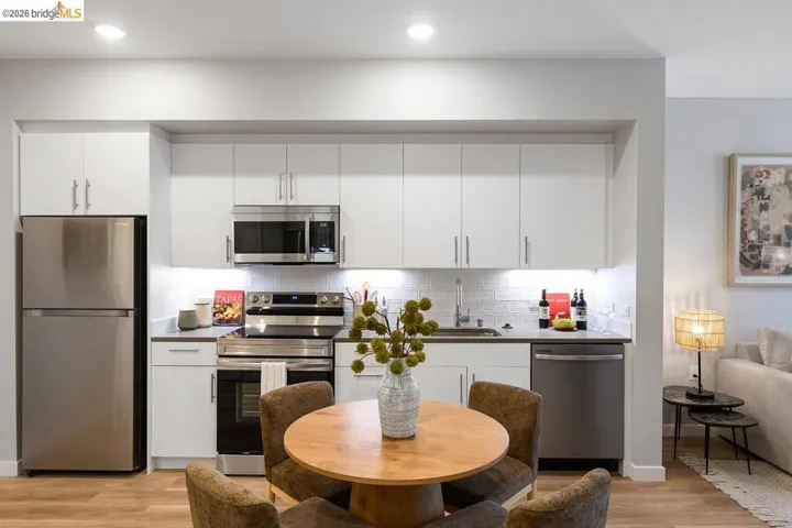 Kitchen featuring tasteful backsplash, appliances with stainless steel finishes, white cabinets, light wood-type flooring, and dark countertops
