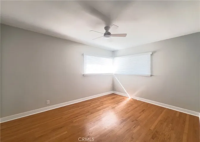  Bedroom 1 with Closets: Comfortable bedroom with rich hardwood floors, a modern ceiling fan, and two closets — including a walk-in style reach-in with rod and shelf — providing excellent storage. A large window brings in natural light while maintaining privacy with clean white blinds.