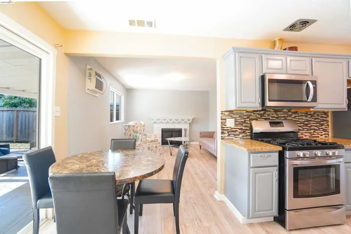 Kitchen featuring stainless steel appliances, light stone countertops, light wood-style flooring, a fireplace, and decorative backsplash