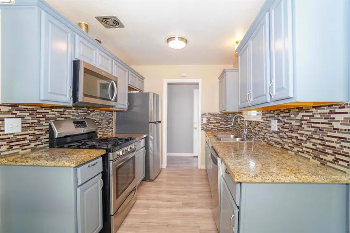 Kitchen with stainless steel appliances, light stone countertops, gray cabinets, and light wood-type flooring