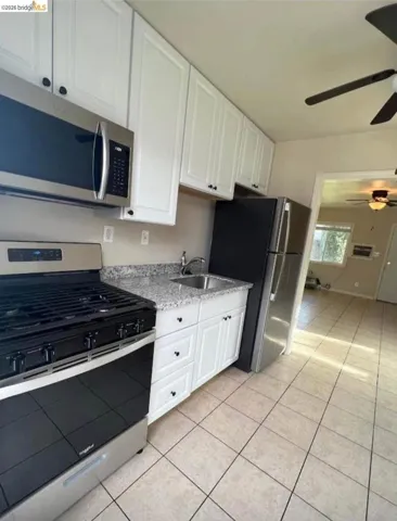 Kitchen with stainless steel appliances, white cabinets, ceiling fan, and light tile patterned floors