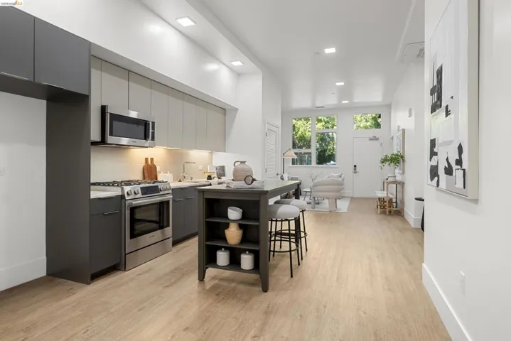 Kitchen with gray cabinets, modern cabinets, appliances with stainless steel finishes, light wood finished floors, and tasteful backsplash