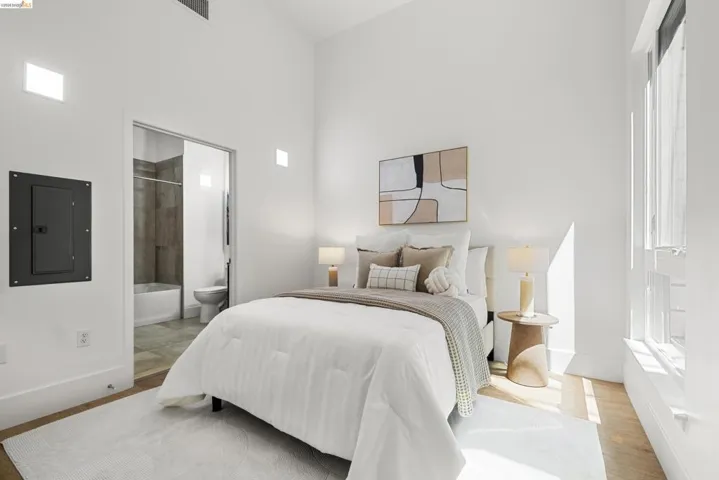 Bedroom featuring electric panel, light wood finished floors, a high ceiling, and connected bathroom