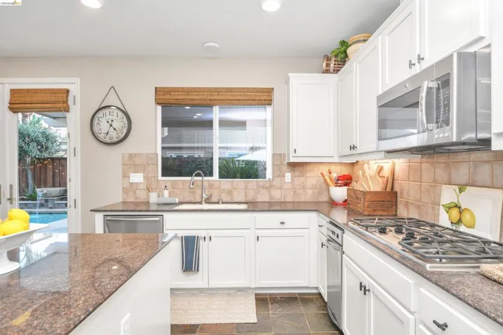 Kitchen featuring white cabinetry, stainless steel appliances, backsplash, dark stone countertops, and recessed lighting