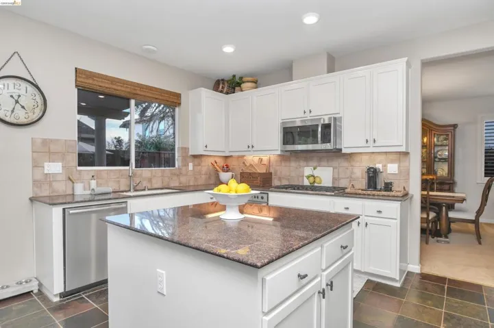 Kitchen featuring dark stone countertops, stainless steel appliances, white cabinetry, a kitchen island, and backsplash
