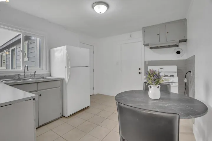 Kitchen with white appliances, light countertops, range hood, light tile patterned floors, and gray cabinets