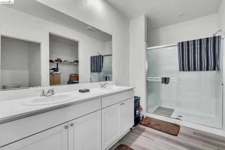 Full bathroom with a shower stall, double vanity, a walk in closet, and light wood-style flooring