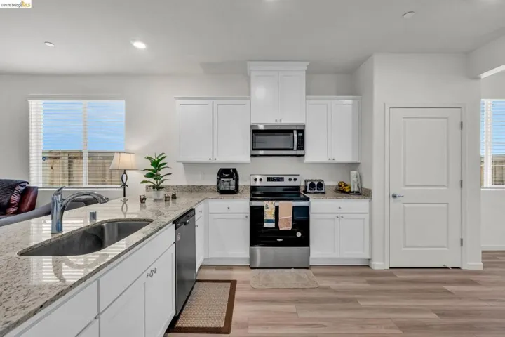 Kitchen featuring stainless steel appliances, white cabinets, light stone countertops, and recessed lighting