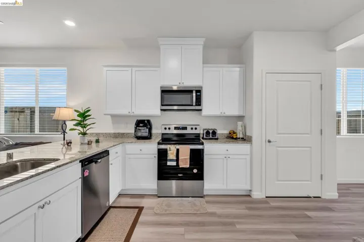 Kitchen with stainless steel appliances, white cabinetry, light stone counters, light wood-type flooring, and recessed lighting