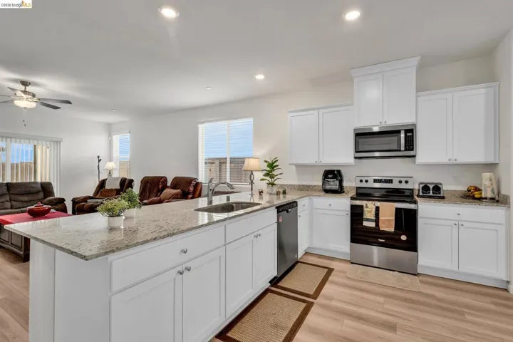 Kitchen with stainless steel appliances, light stone countertops, white cabinets, a peninsula, and recessed lighting