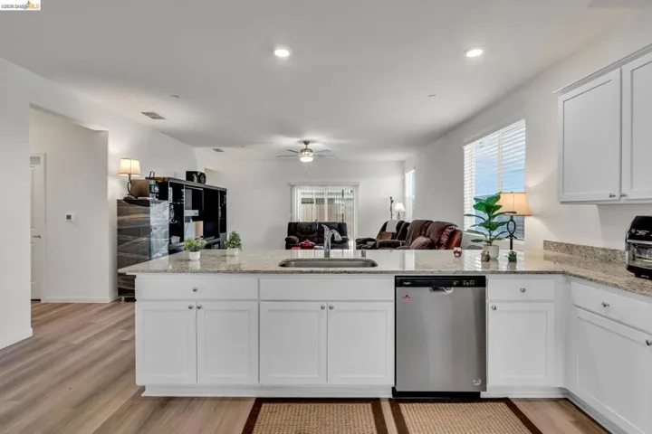 Kitchen featuring a peninsula, open floor plan, dishwasher, light stone counters, and a ceiling fan