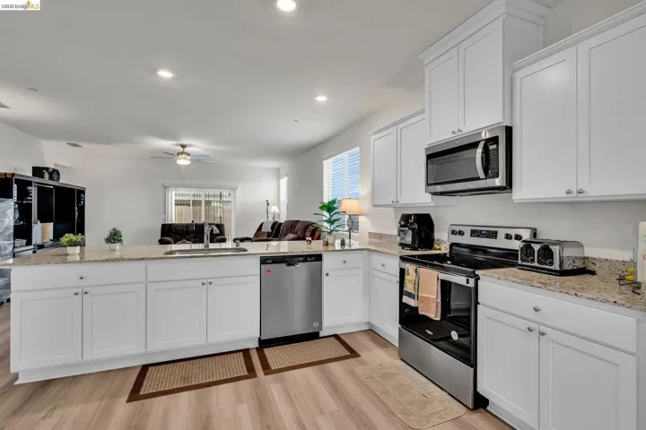 Kitchen with stainless steel appliances, white cabinetry, light stone countertops, open floor plan, and a peninsula