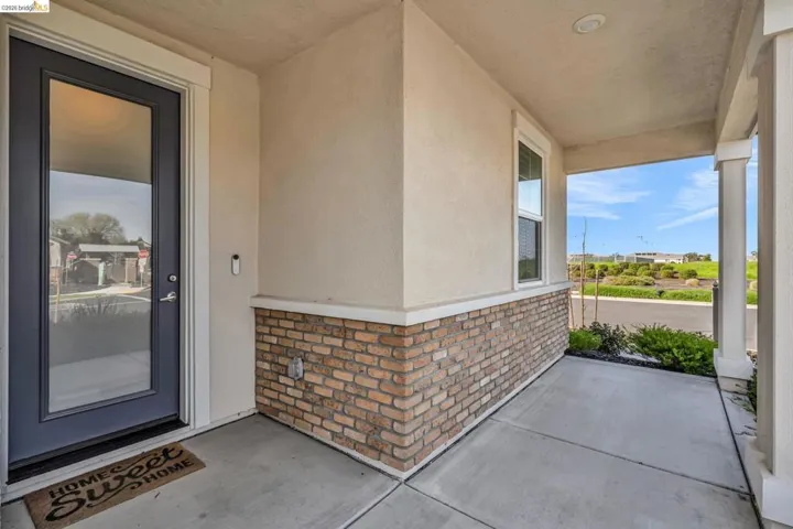 Doorway to property featuring brick siding, covered porch, and stucco siding