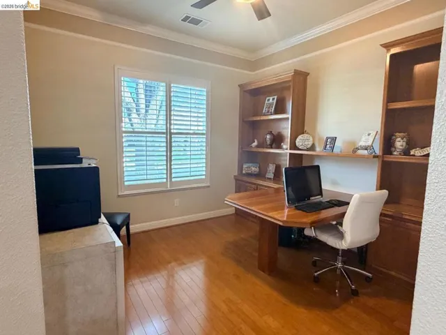 Office area with light wood-style floors, a ceiling fan, ornamental molding, and built in shelves