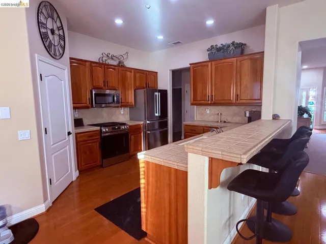 Kitchen with tile counters, a peninsula, stainless steel appliances, wood finish cabinets, and recessed lighting