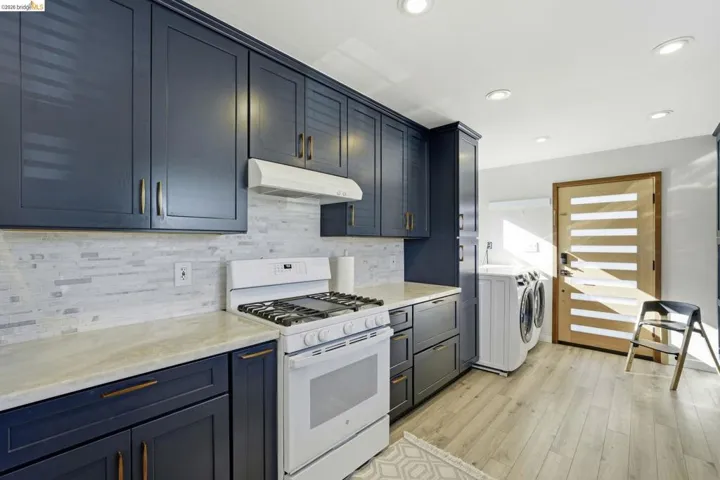 Kitchen with white gas range, light wood finished floors, separate washer and dryer, recessed lighting, and backsplash