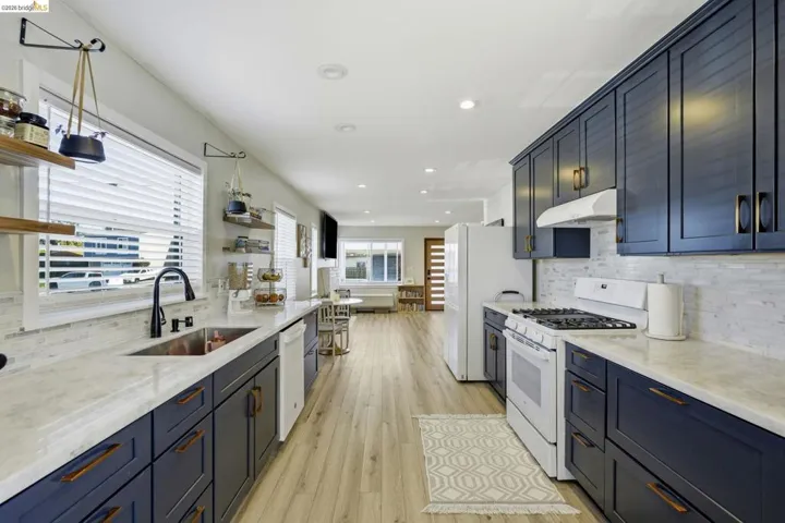Kitchen featuring white appliances, backsplash, open shelves, light stone counters, and blue cabinetry