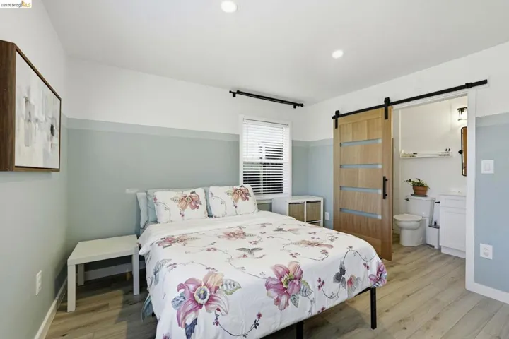 Bedroom with a barn door, light wood-style floors, ensuite bath, and recessed lighting