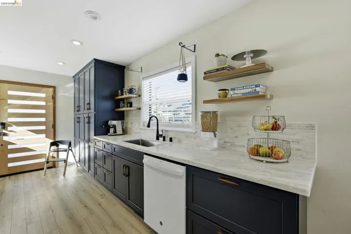 Kitchen with white dishwasher, light stone countertops, open shelves, light wood-type flooring, and recessed lighting