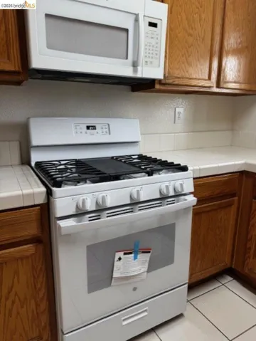Kitchen featuring tile counters, white appliances, wood finish cabinets, and light tile patterned floors