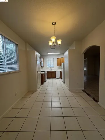 Kitchen featuring light tile patterned floors, wood finish cabinetry, hanging lights, arched walkways, and light countertops
