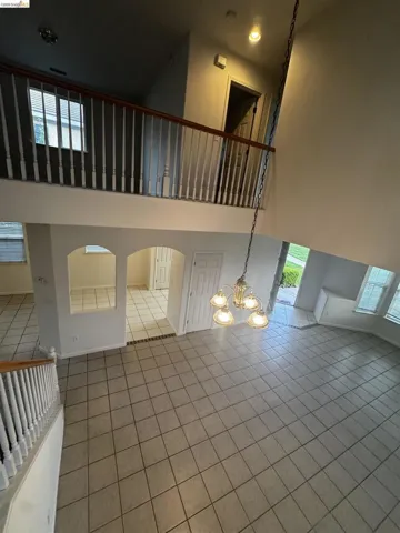 Unfurnished living room with a high ceiling, tile patterned floors, arched walkways, and hanging lights
