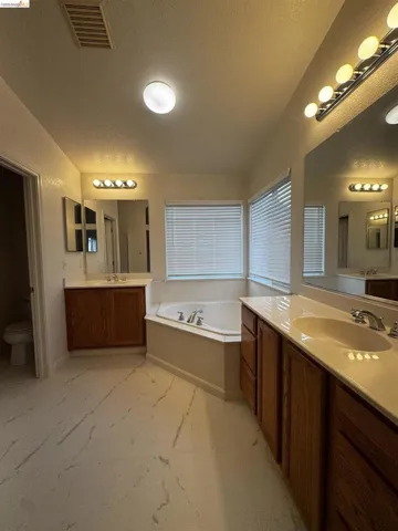 Bathroom with two vanities, a garden tub, and a textured wall