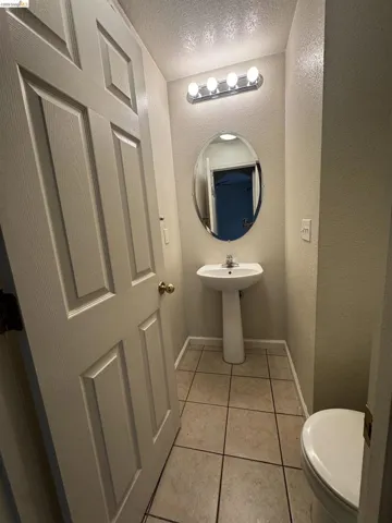 Bathroom with a textured wall, a textured ceiling, and light tile patterned floors