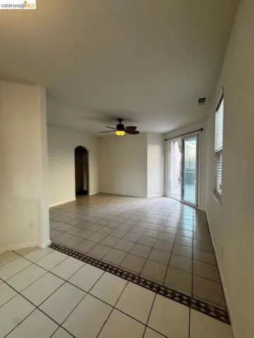 Empty room featuring arched walkways, light tile patterned flooring, and a ceiling fan