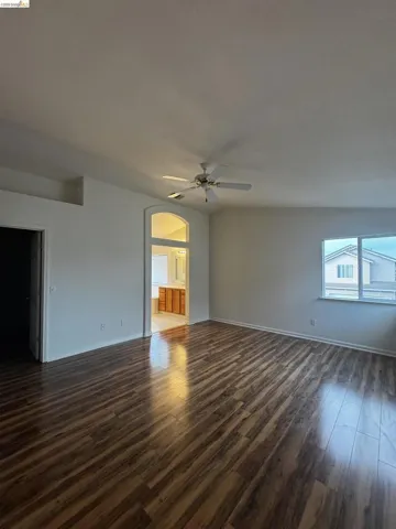 Empty room with dark wood finished floors, a ceiling fan, plenty of natural light, and arched walkways