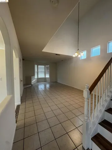 Unfurnished living room with light tile patterned flooring, a high ceiling, and a chandelier