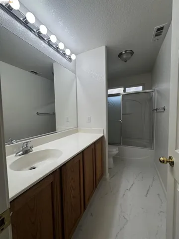 Bathroom featuring vanity, bath / shower combo with glass door, a textured ceiling, and light marble finish flooring