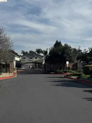View of asphalt road with a gated entry, a gate, and curbs