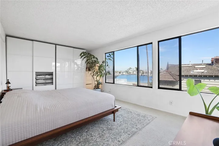 Unit #64 - Primary Suite has panoramic windows with a view of Alamitos Bay, glass panel closet doors and carpet flooring.