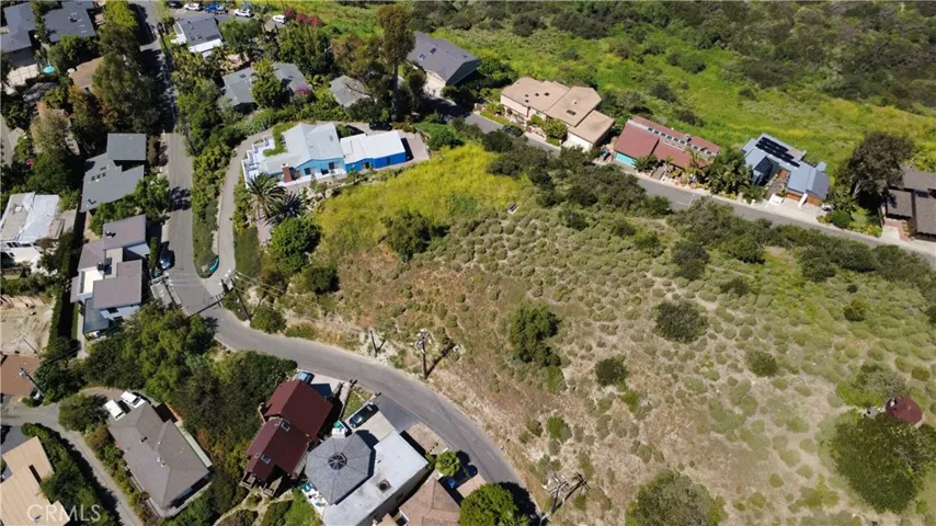 Wide aerial perspective capturing the surrounding neighborhood and coastal hillside setting, reinforcing the vision for a private, design-forward home.