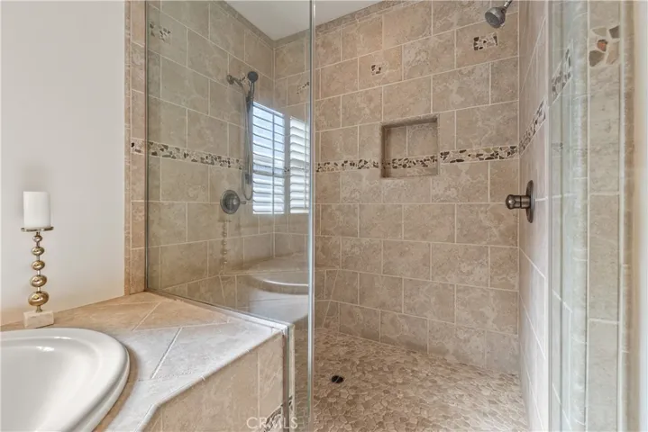 Spacious glass-enclosed shower with stone tile surround, decorative accents, and built-in vanity.